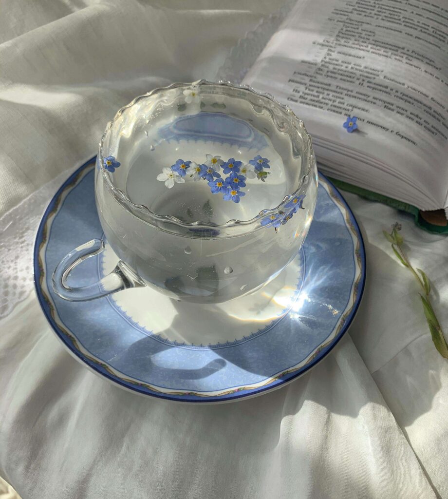 Glass cup of clear tea with floating blue flowers next to an open book, symbolizing calm reflection and personal growth during eating disorder recovery.